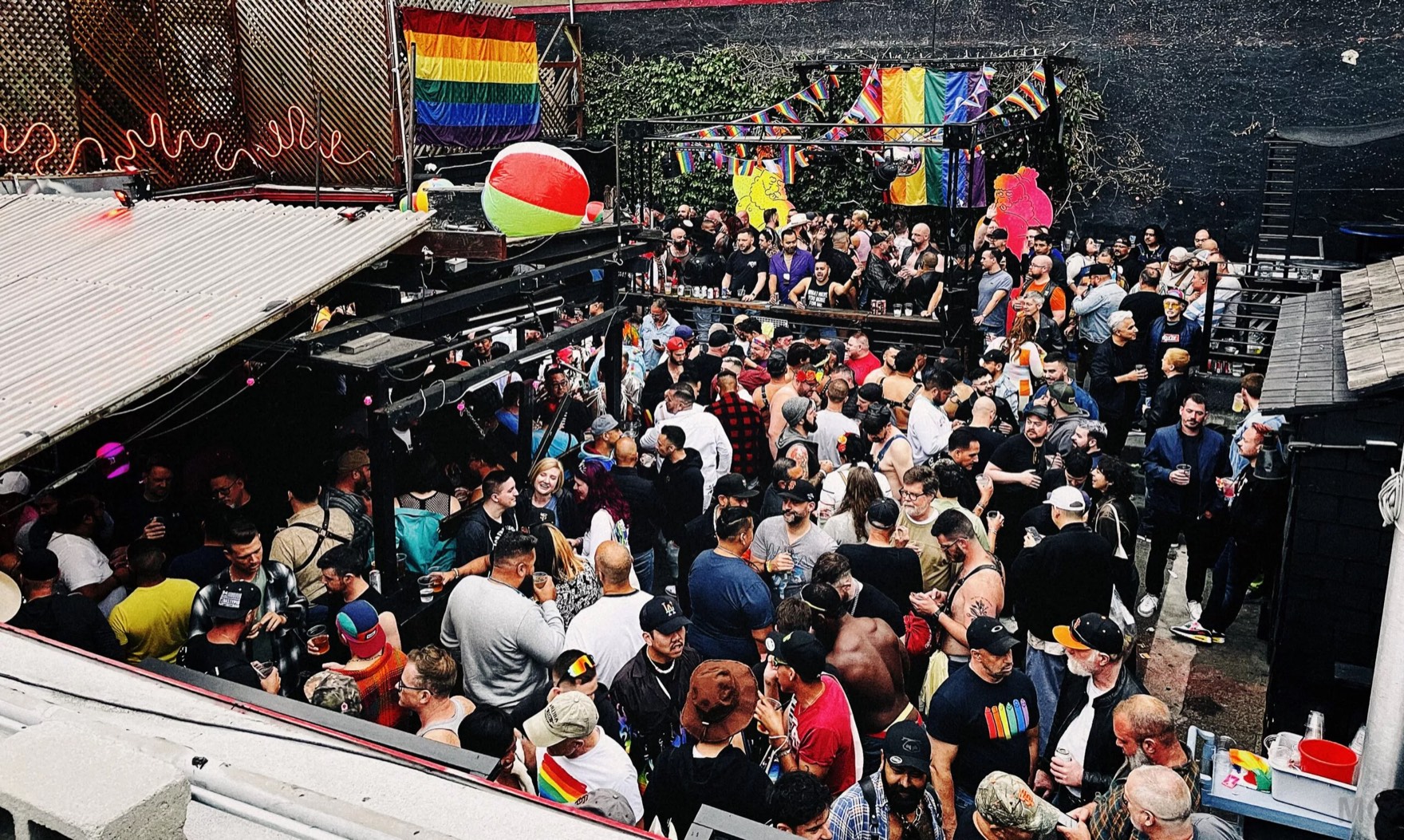 A packed Sunday Beer Bust on the SF Eagle's outdoor patio, with the stage, pride flags, and string lights above the crowd